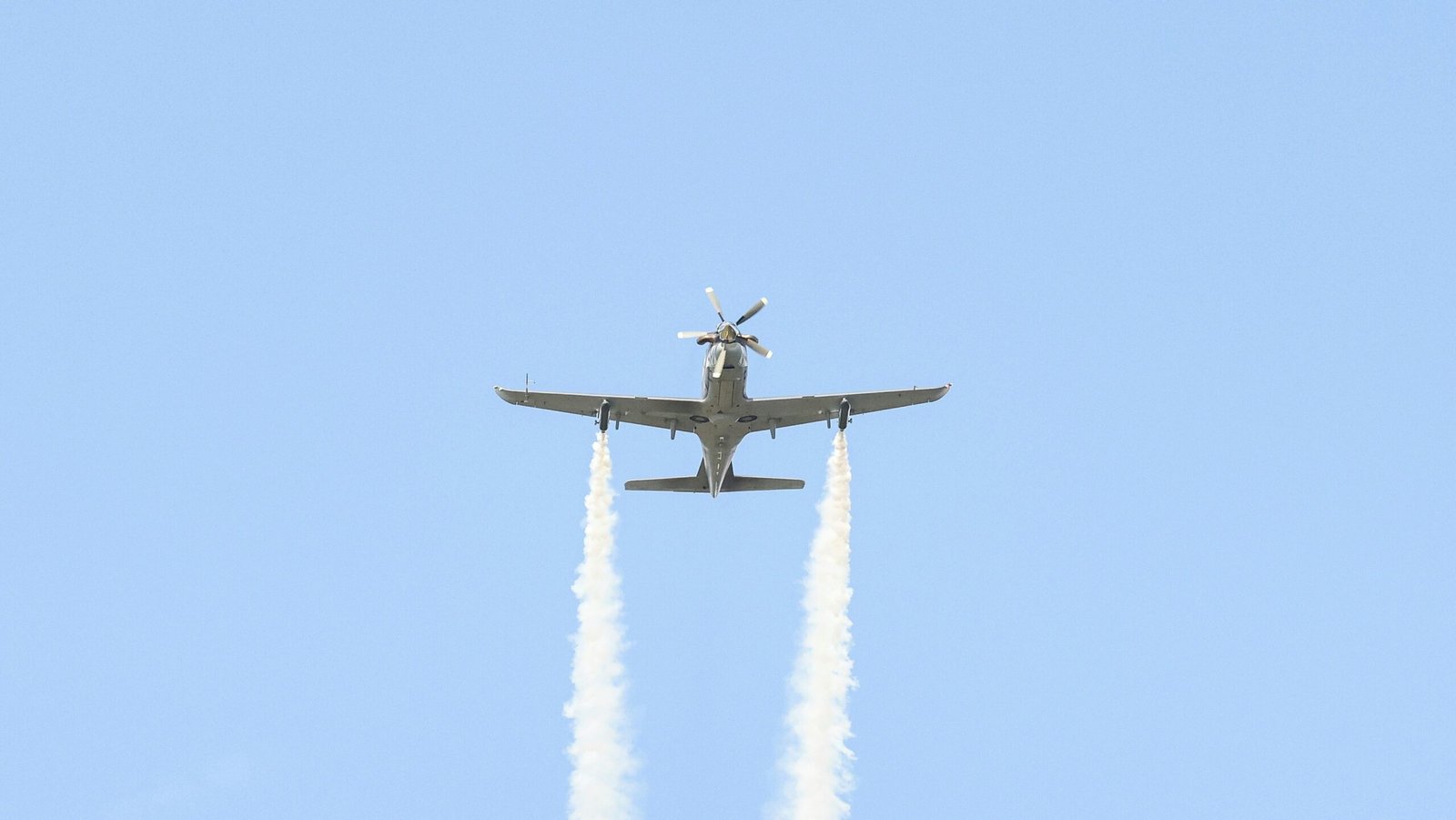A plane flying in the air with two smoke trails behind it